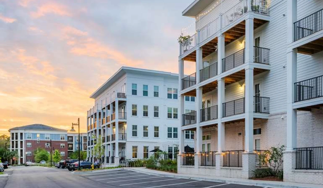Apartment community with white siding, wraparound balconies, and warm sunset sky in background