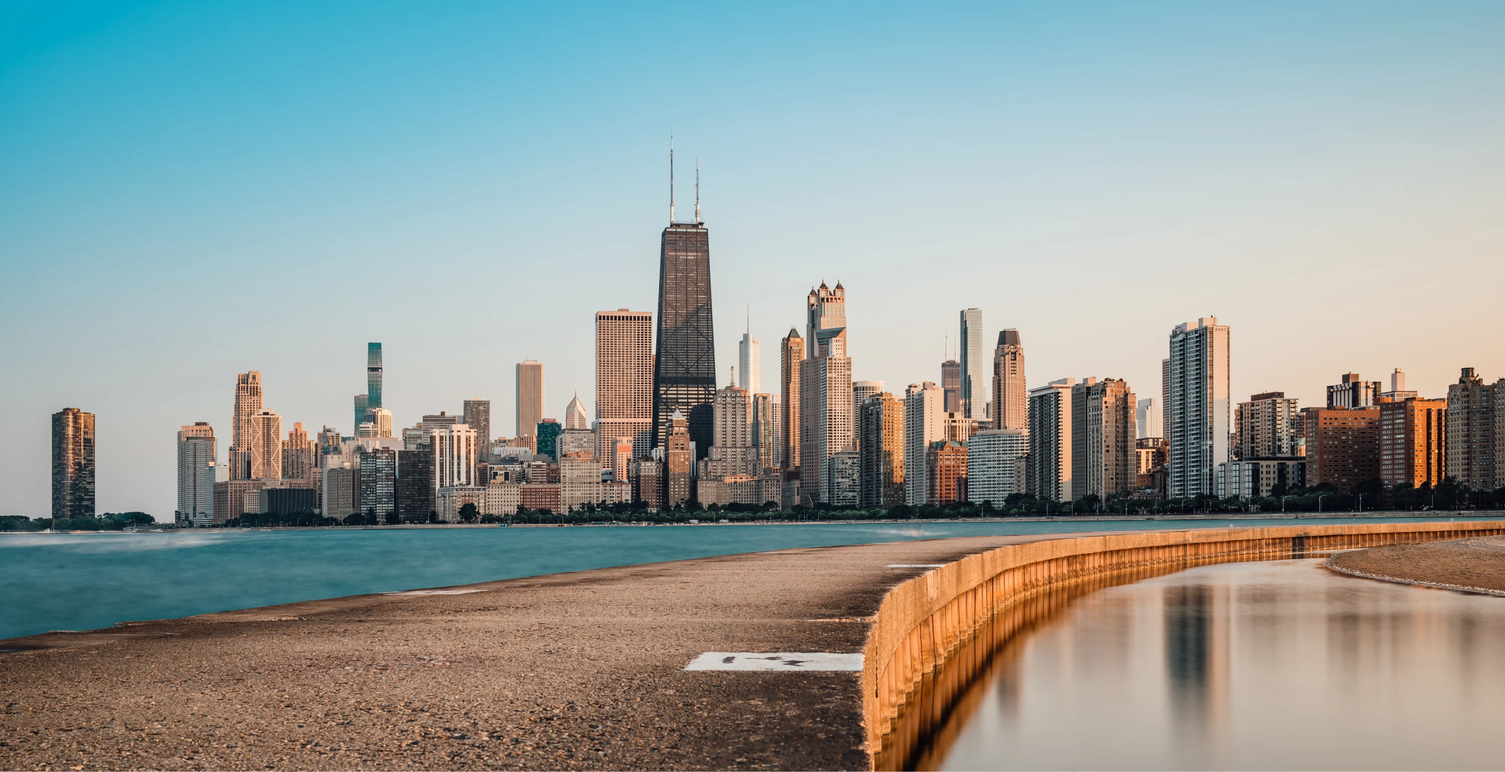 Scenic view of Chicago skyline at sunset with Hancock Center and calm Lake Michigan foreground